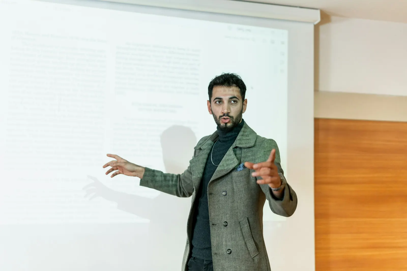 Spreker tijdens een lezing, gebarend voor een projectiescherm.